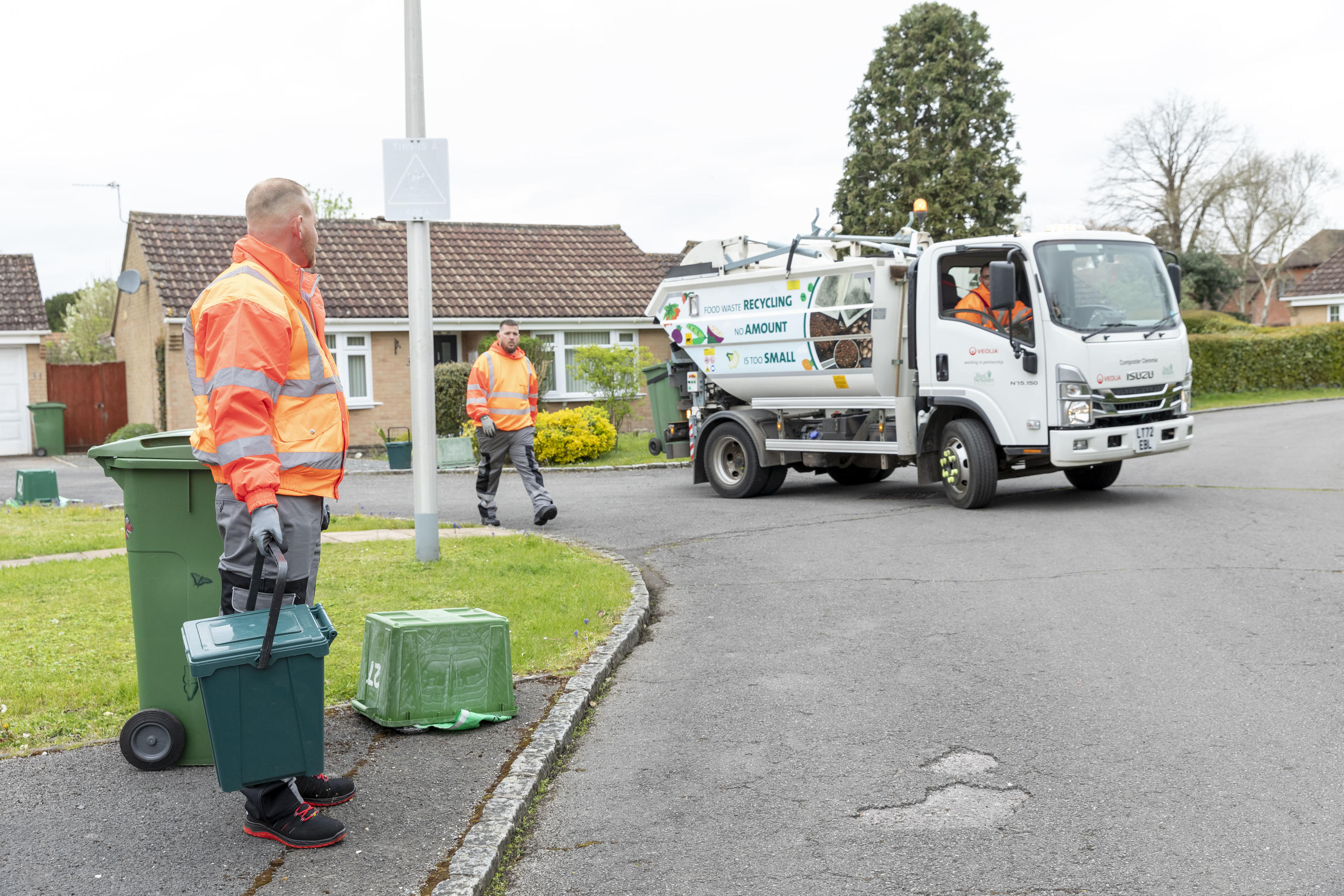 Two loaders work along a road picking up bins to empty into the vehicle waiting in the road.